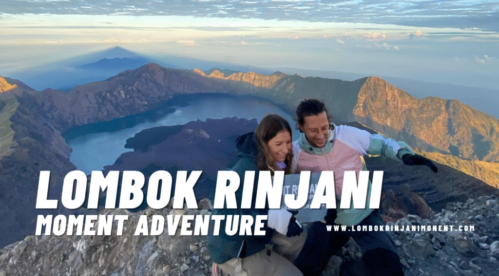 A jubilant couple on the Mount Rinjani summit/rim at sunrise, with the entire caldera and Segara Anak lake visible behind them. The mountain's shadow stretches far across the horizon.
