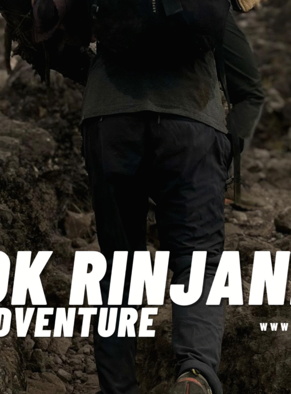 A hiker seen from behind, struggling to ascend a steep, rocky section of the trail towards the Senaru Crater Rim on Mount Rinjani, showing only the lower body and backpack.