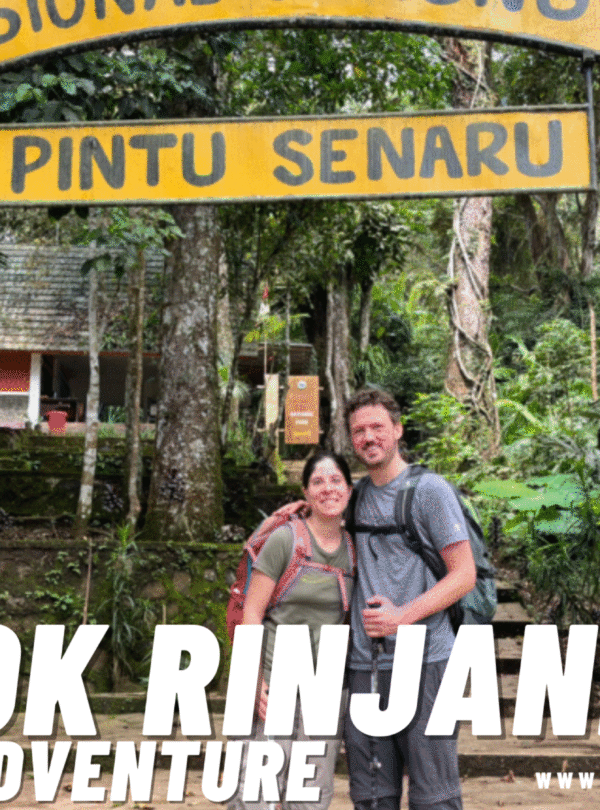 A smiling couple of hikers under the "Taman Nasional Gunung Rinjani - Pintu Senaru" gate, surrounded by dense green forest, marking the start or end of the trek.