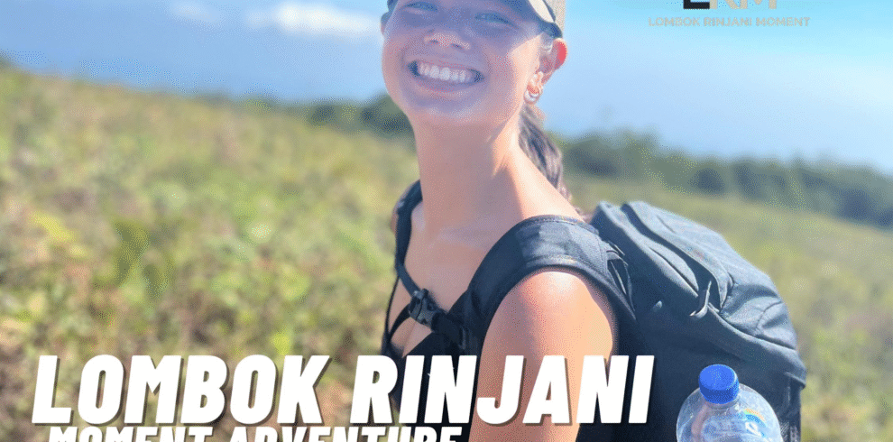A young female hiker smiling brightly and wearing a cap and backpack on a sunny, grassy slope of Mount Rinjani.