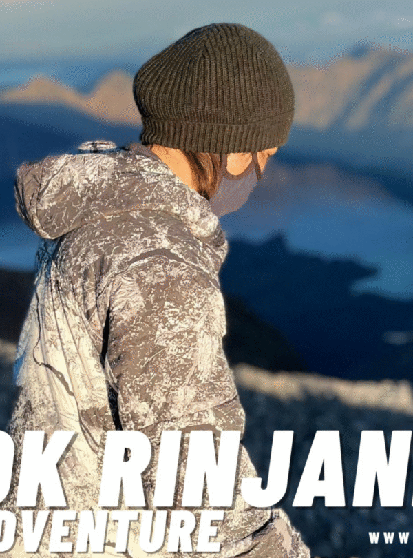 Hiker in a beanie and patterned jacket looking out over the Rinjani caldera and Segara Anak lake.