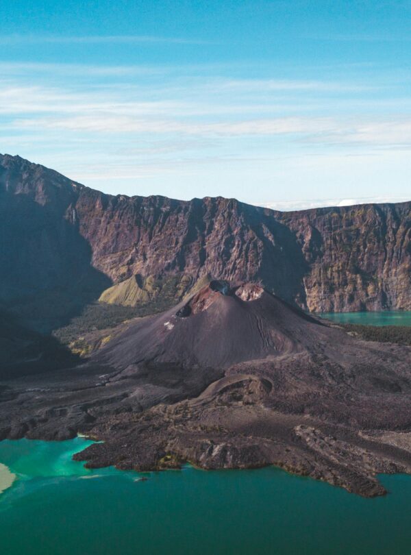 Aerial view of the Segara Anak crater lake and the Gunung Barujari cone within the massive caldera of Mount Rinjani, Lombok. The lake shows vibrant turquoise and yellowish-green water.
